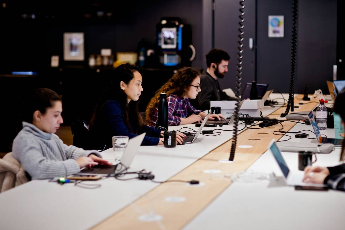 a group of people sitting at a table with laptops
