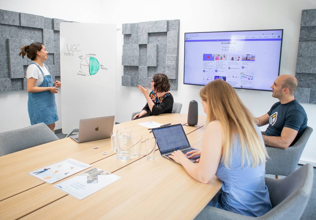 A woman presenting User-Generated Content results to the marketing team in a meeting room with a white board and a screen