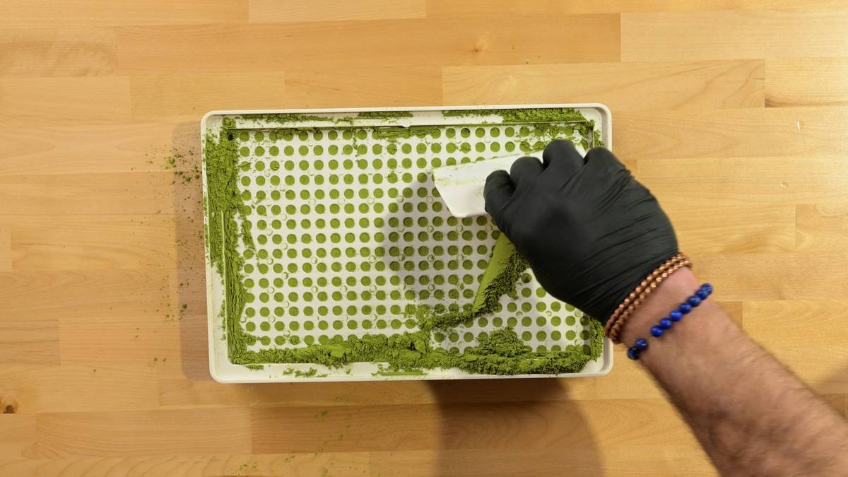 Spreading herbal green powder into empty capsules using a Cap & Press™ Core Series 400 Hole capsule filling machine from a top overhead view - Photo courtesy of https://blated.com - credit appreciated